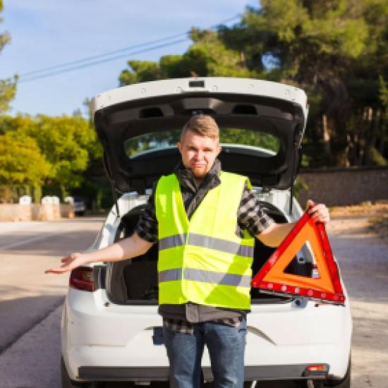 Un homme et sa voiture sur la route portant un gilet jaune et un triangle de signalisation