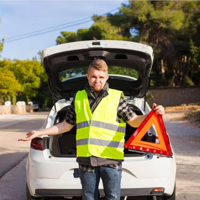 Un homme et sa voiture sur la route portant un gilet jaune et un triangle de signalisation